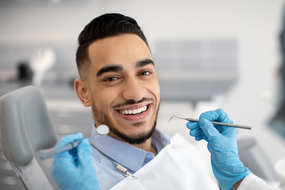 smiling patient in dental chair while dentist holds dental tools